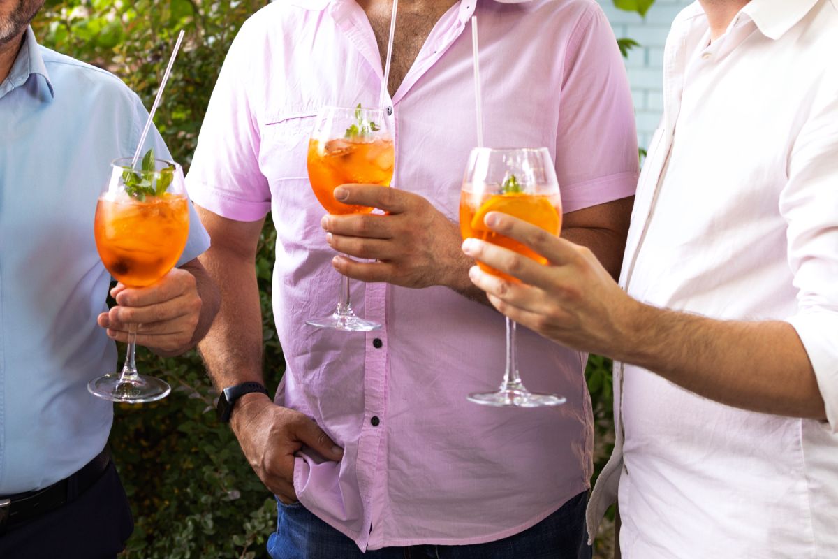 Male friends spending time together, drinking Aperol spritz cocktail on summer party. Talking together