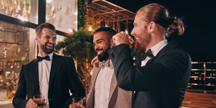 Three happy men in suits holding glasses with whiskey while spending time on party
