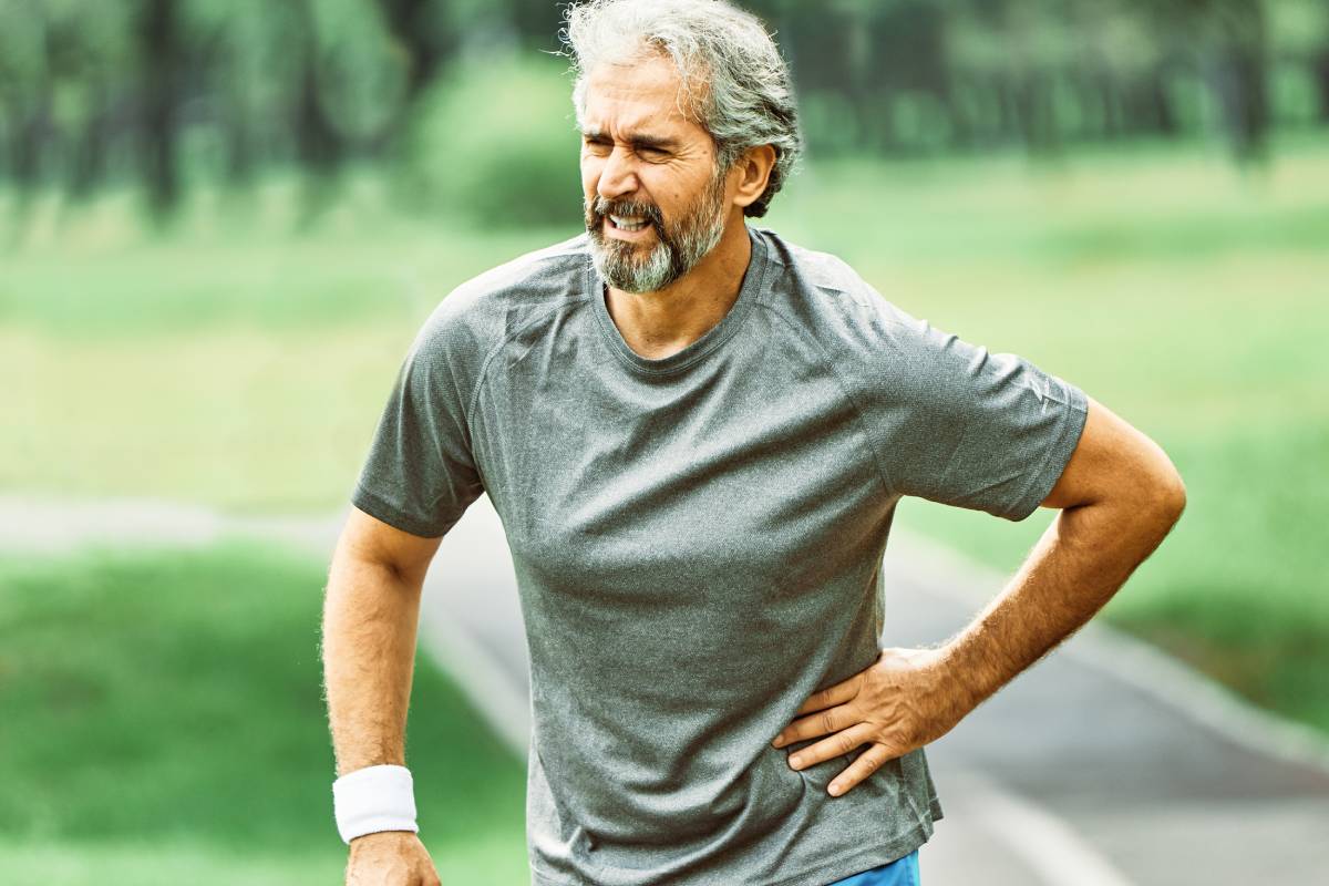 portrait of a senior man exercising and running outdoors having chest or stomack or hip or back pain or injury