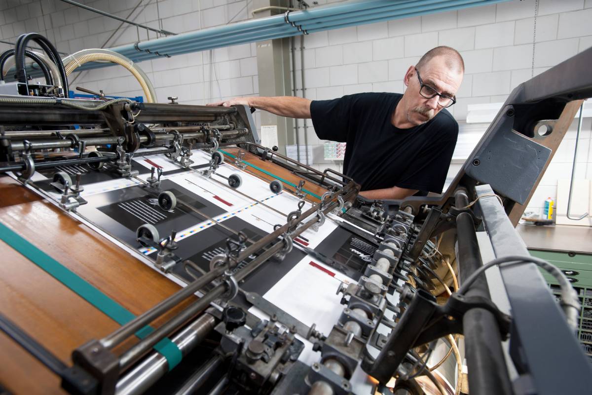 Worker monitoring print machine in printing workshop