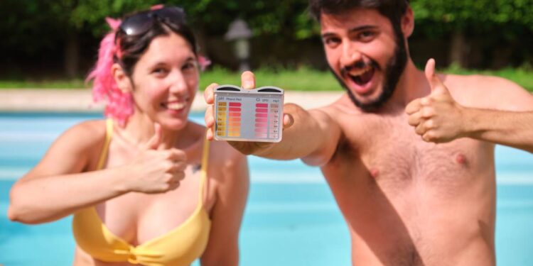 Young happy couple giving the ok to the ph and cl levels of their swimming pool. Summertime.
