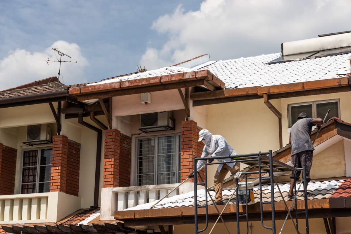 Worker adding undercoat foundation paint onto rooftop with roller as primer at residential building in renovation