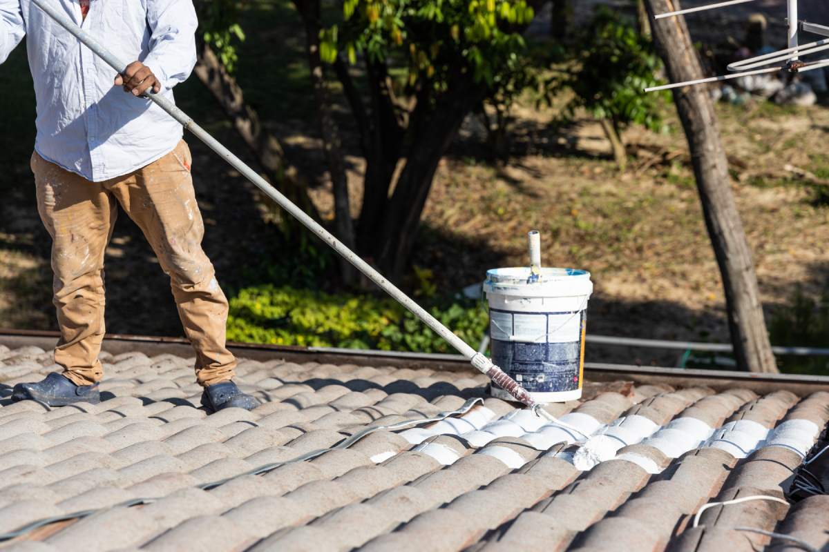 Worker adding undercoat foundation paint onto rooftop with roller as primer at residential building in renovation