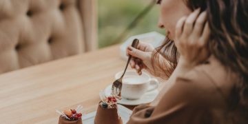Crop photo of woman eating double tiramisu dessert decorated with fresh berries at the cafe